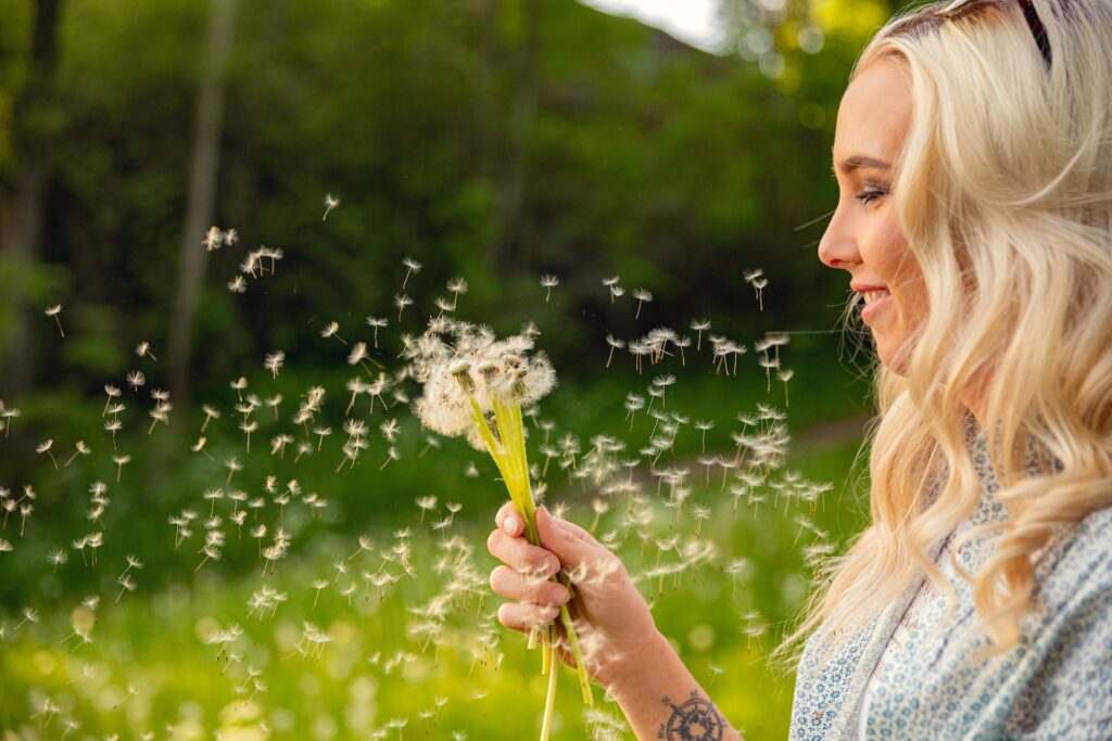 Closeup of young woman looking at flying dandelion seeds in forest during sunset