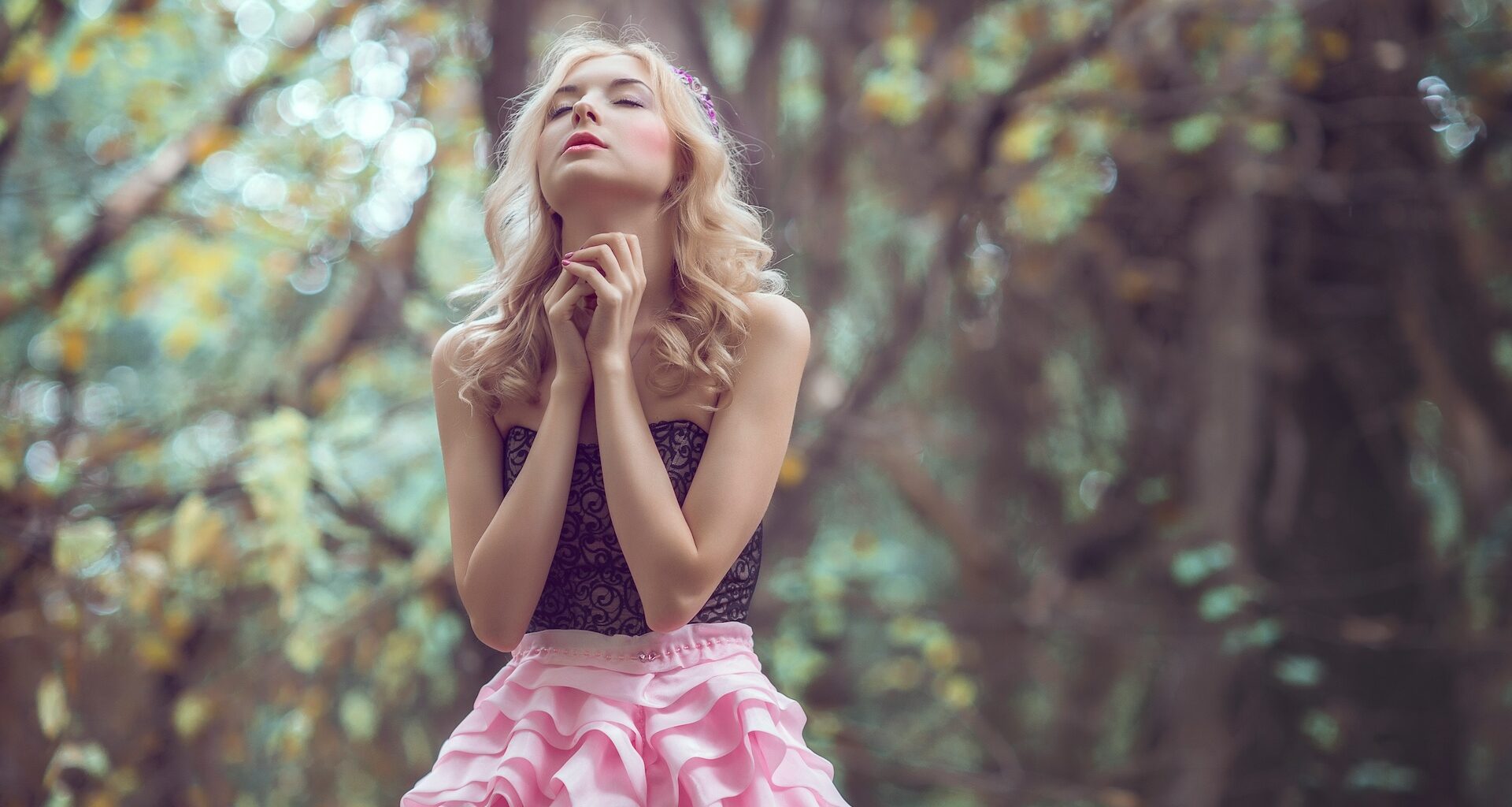 Closeup of young woman looking at flying dandelion seeds in forest during sunset